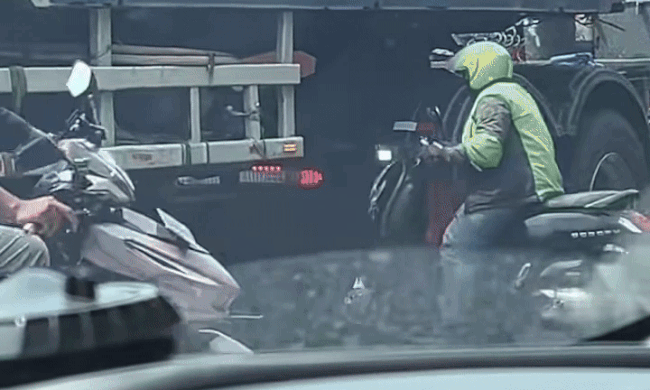 Người đi xe máy chui qua gầm xe container khi tắc đường