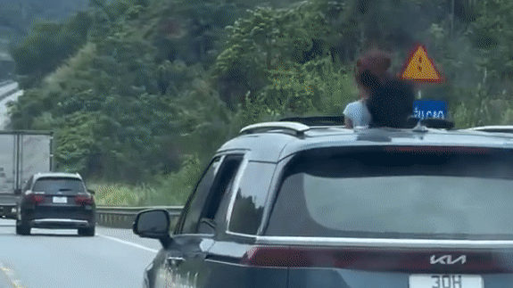 Hai người thò đầu qua cửa sổ trời trên đường cao tốc